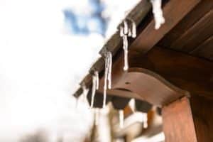 Hanging icicles from the roof of a wooden building on a winter frosty day, a lot of snow on the roof